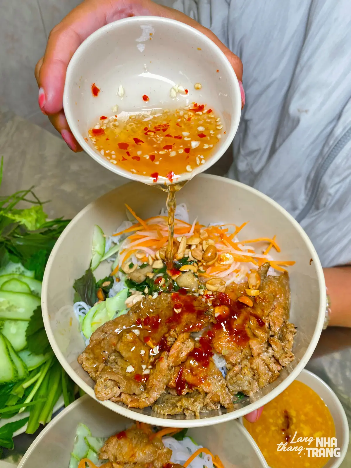 Rice noodle bowl with grilled pork, herbs and sweet chilli fish sauce being poured over