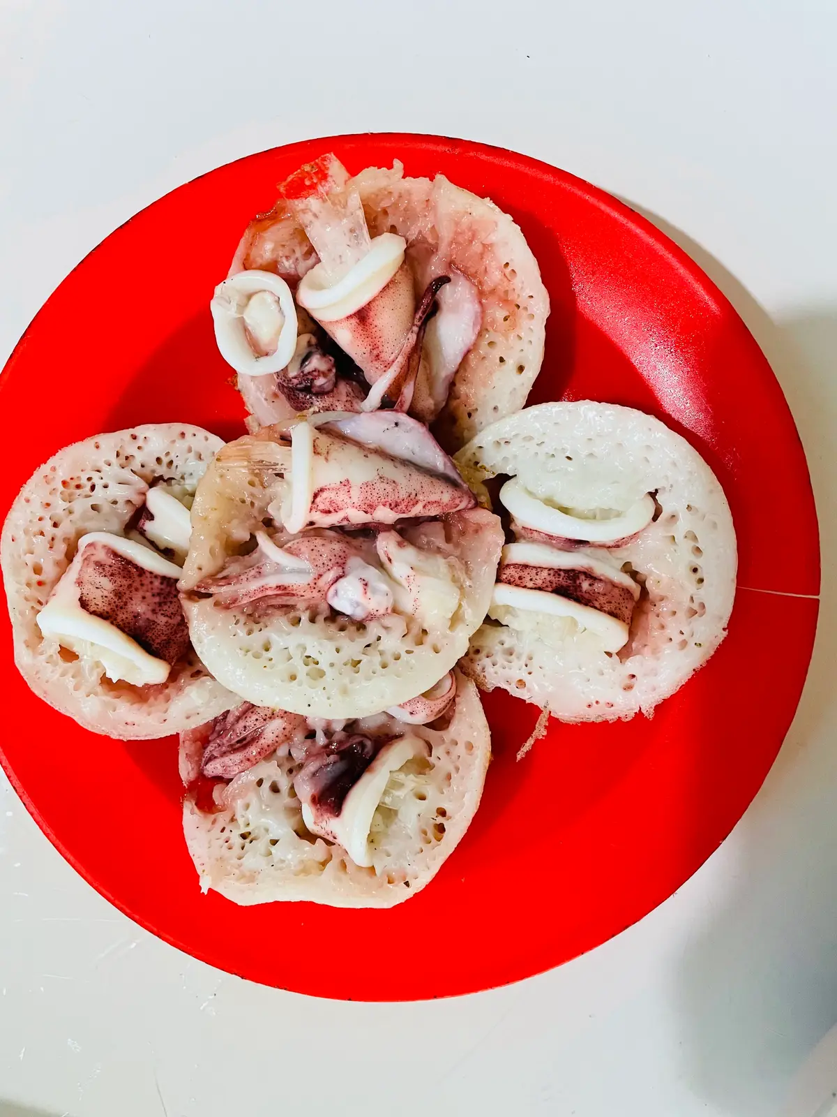 Plate of rice pancakes topped with sliced squid on a red plate