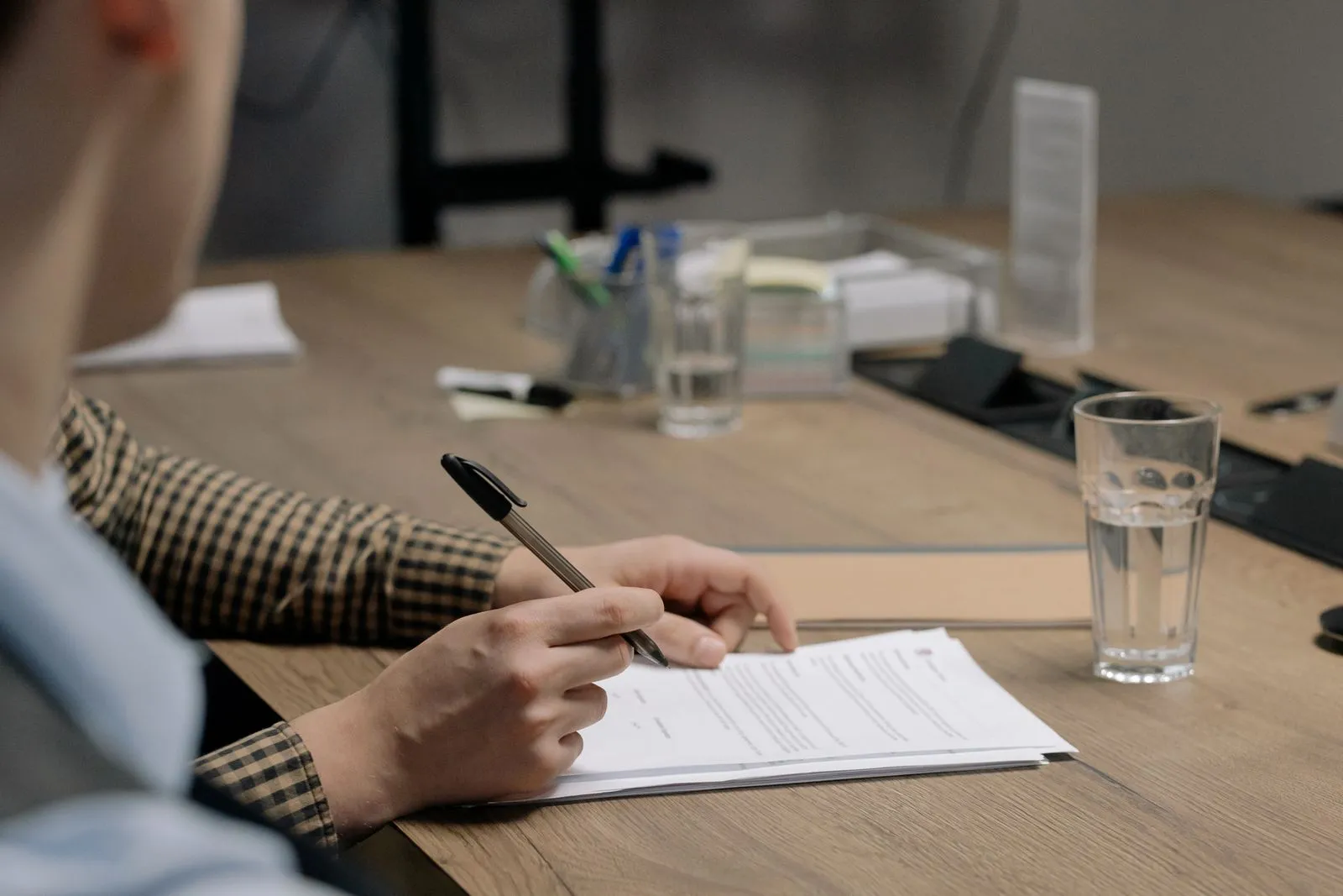 A person at a meeting table signing a printed document, a glass of water beside it